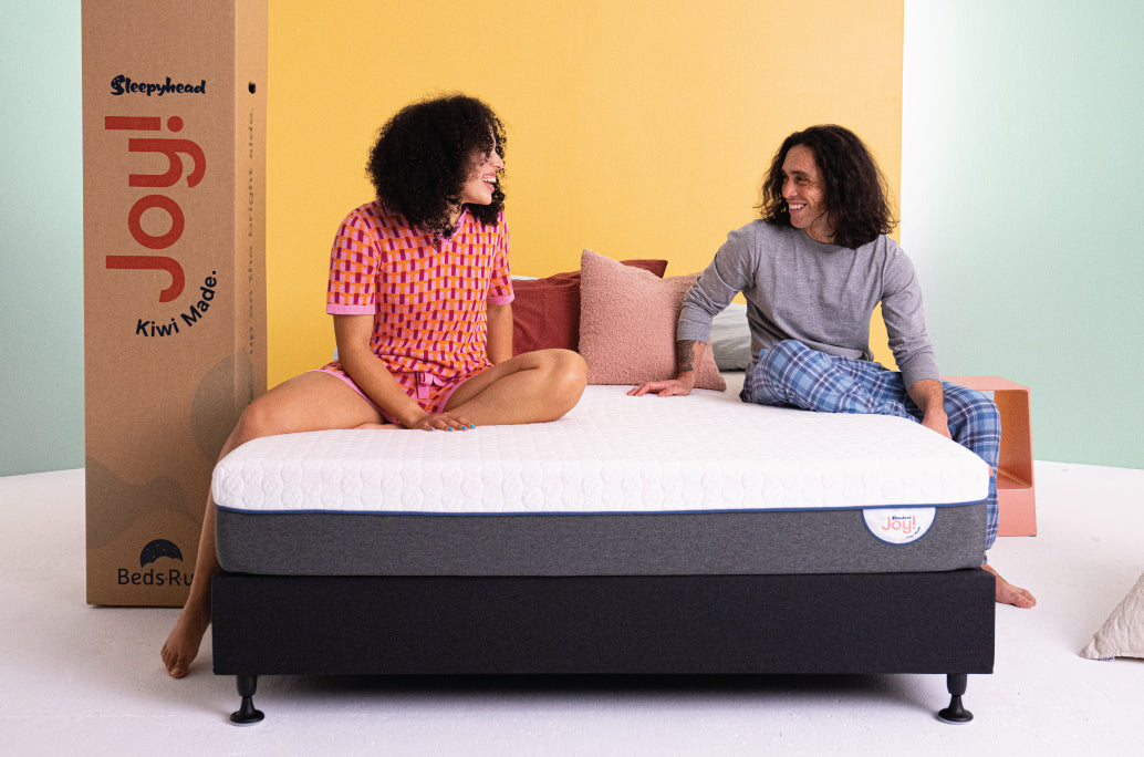 Happy couple sitting on the Joy Mattress - Enjoying comfort and support